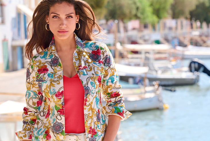 model wearing a status print white denim jacket, hot coral top, white leather belt, and white jeans.